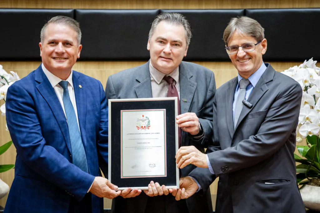 Os deputados Altair Silva (esquerda) e Neodi Saretta (direita), entregaram uma placa comemorativa a Everton Luis Krabbe, da Embrapa Suínos e Aves. (Fotos: Bruno Collaço / AGÊNCIA AL)